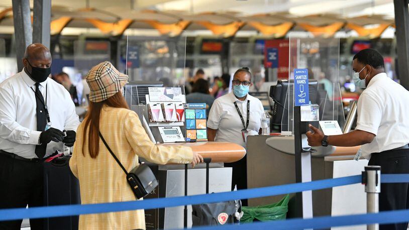 Travelers wearing face masks check in through plexiglass dividers at Delta Airline at Hartsfield-Jackson International Airport on Thursday, July 2, 2020.(Hyosub Shin /Hyosub.Shin@ajc.com)