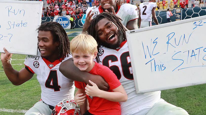 Georgia players James Cook ( left), Isaiah Wilson (top) and Solomon Kindley (right)  celebrate a 52-7 victory over Georgia Tech with head coach Kirby Smart's son Andrew in a NCAA college football game on Saturday, November 30, 2019, in Atlanta.  Curtis Compton/ccompton@ajc.com