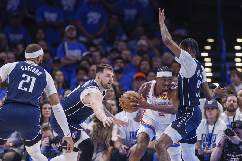 Oklahoma City Thunder guard Shai Gilgeous-Alexander, center, tries to pass the ball to a teammate as Dallas Mavericks center Daniel Gafford (21), guard Luka Doncic, second from left, and forward Derrick Jones Jr. defend during the first half of Game 1 of an NBA basketball second-round playoff series, Tuesday, May 7, 2024, in Oklahoma City. (AP Photo/Nate Billings)