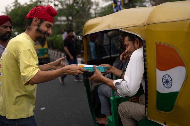 A supporter of the Aam Aadmi Party distributes sweets to a passenger as he waits with others for the release of the party leader Arvind Kejriwal from Tihar Jail in New Delhi, India, Friday, May 10, 2024. The Supreme Court ordered Arvind Kejriwal's temporary release enabling him to campaign in the country's national election until the voting ends on June 1. (AP Photo /Altaf Qadri)
