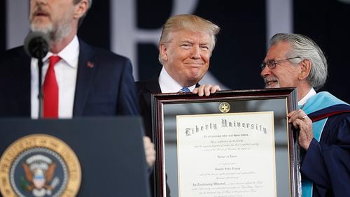 President Donald Trump, center, is presented an Honorary Degree by Ronald E. Hawkins, right, Provost and Chief Academic Officer, before giving the commencement address for the Class of 2017 at Liberty University in Lynchburg, Va., Saturday, May 13, 2017. Speaking at the podium is Liberty University President Jerry Falwell, left.