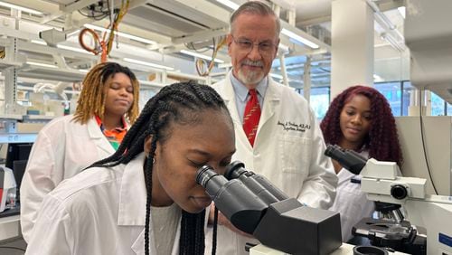 Dr. Barney Graham watches with Morehouse School of Medicine students Briana Brock, left and Dana Battle, right, as Morehouse School of Medicine student Aww Sore looks into a microscope .