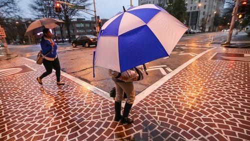 Nisha George (left) and LaTonia Evans try to stay dry Wednesday at the Peachtree Center. JOHN SPINK / JSPINK@AJC.COM