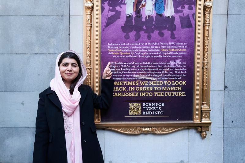 This photo provided by Rubenstein shows Malala Yousafzai pointing to a sign for her off-Broadway musical “Suffs” in New York. Yousafzai and former Secretary of State Hillary Rodham Clinton are joining together as producers of the musical about the suffragist movement. (Jenny Anderson via AP)