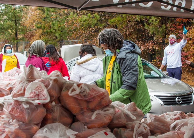 Food bank volunteers, including Steve Gordon, green jacket, bundle sweet potatoes and distribute dry goods, fresh fruits and vegetables, and frozen meats to those waiting in long lines at Jefferson Park Recreation Center in East Point. (Jenni Girtman for The Atlanta Journal-Constitution)