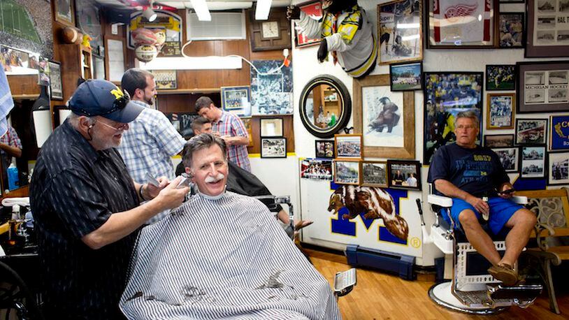 Jerry Erickson gives a haircut at his Coach and Four Barber Shop in Ann Arbor, Mich., July 22, 2015. Jim Harbaugh’s return to the University of Michigan, where he is set for his first home game in charge, has re-energized longtime fans, including those at this barbershop, once a favored haunt of the Wolverines' legendary coach Bo Schembechler. (Laura McDermott/The New York Times)