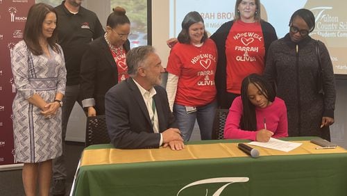 Fulton County Superintendent Mike Looney (seated, left) watches Hopewell Middle School eighth grader Farrah Brown sign a REACH contract, committing to good attendance, behavior and grades in order to obtain the $10,000 college scholarship. Her mother, Prima Wituka, is on the right. (Courtesy of Fulton County Schools)