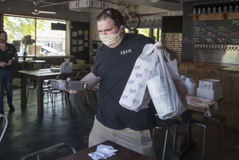 In downtown Lilburn, 1910 Public House restaurant server/bartender Greg Thompson prepares a curbside pickup of a customer order: a meal and grocery staples such as toilet paper. (ALYSSA POINTER / ALYSSA.POINTER@AJC.COM)