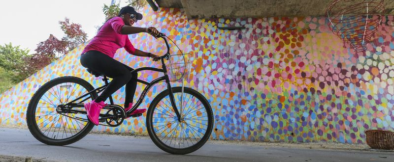 Monique Lee of College Park rides her bike along the Beltline near Piedmont Park. The mural behind her was painted by Alex Brewer. Also known as the artist Hense, he has several colorful murals in the Atlanta area. One of the most popular murals is this one under Virginia Avenue near Piedmont Park. JOHN SPINK /JSPINK@AJC.COM
