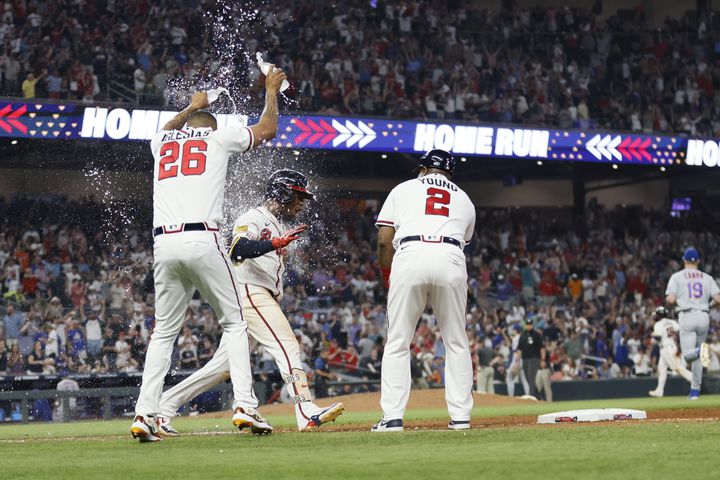 The game-winning celebration for Albies began as he rounded first base and received a splash of water from Raisel Iglesias as he prepares for his hand-slap with first-base coach Eric Young. (Miguel Martinez / miguel.martinezjimenez@ajc.com 