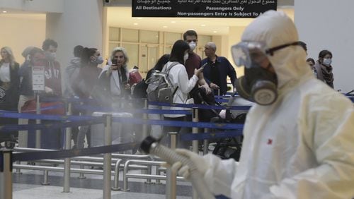 Passengers line up as workers wearing protective gear spray disinfectant as a precaution against the coronavirus outbreak, in the departure terminal at the Rafik Hariri International Airport, in Beirut, Lebanon, Thursday, March 5, 2020. The novel coronavirus has infected more than 80,000 people globally, causing around 2,700 deaths, mainly in China. (AP Photo/Hassan Ammar)