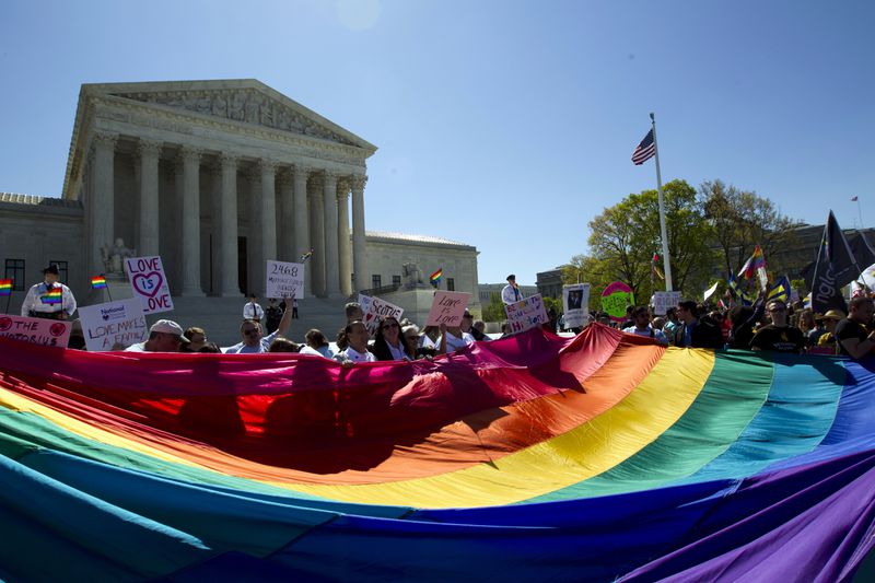  In this April 28, 2015, file photo, demonstrators stand in front of a rainbow flag of the Supreme Court in Washington.