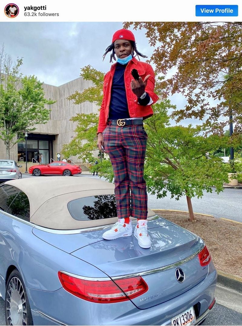 Young Slime Life (YSL) rapper Yak Gotti (Deamonte Kendrick) stands on the car of rival rapper YFN Lucci (Rayshawn Bennett) in a taunting move in an ongoing feud between the groups. Both rappers have been charged in separate racketeering cases.