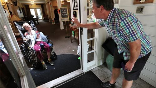 Dan Goerke waves at his wife Denise to get her attention and hopefully a smile by temporarily removing his mask while social distancing from outside during a doorway visit at the Mann House, an Alzheimer's care facility that provides assisted living services on Monday, Aug. 3, 2020, in Sandy Springs. (Curtis Compton ccompton@ajc.com)