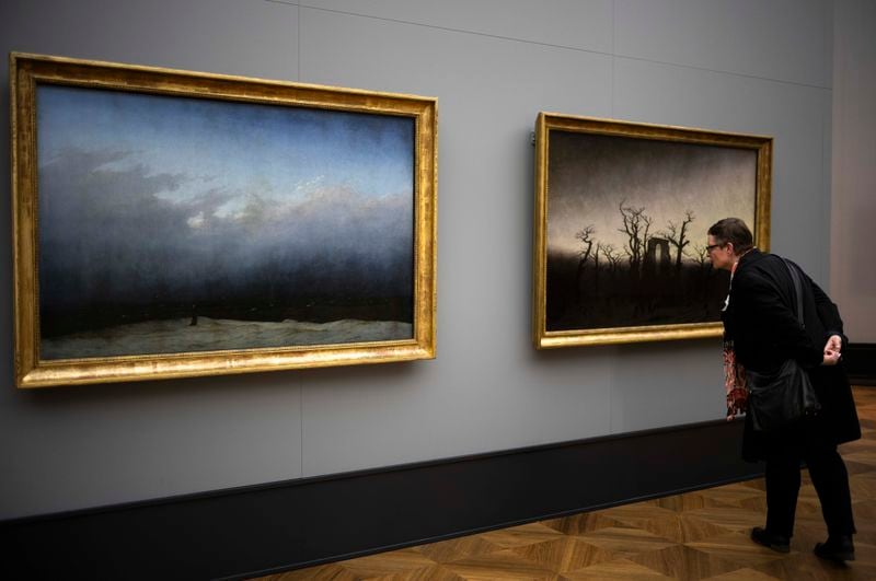 A woman inspects Caspar David Friedrich's painting 'Abby Among The Oaks' whis is displayed next to 'Monk By The Sea' during a press preview of the exhibition 'Caspar David Friedrich. Infinite Landscapes' at the Alte Nationalgalerie museum in Berlin, Wednesday, April 17, 2024. The exhibition marking the 250th birthday of Caspar David Friedrich and will run from April 19 until August 4, 2024. (AP Photo/Markus Schreiber)