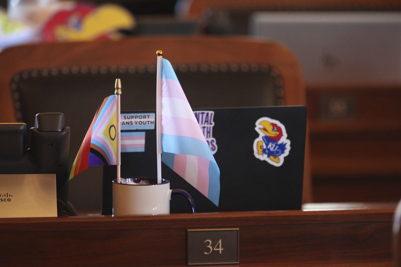 Small transgender rights flags sit on the desk in the Kansas House chamber for Rep. Allison Hougland, D-Olathe, during a break in the House's daylong session, Monday, April 29, 2024, at the Statehouse in Topeka, Kan. Hougland, other Democrats, and a few Republicans have prevented the GOP-controlled Legislature from overriding Democratic Gov. Laura Kelly's veto of a proposed ban on gender-affirming care for transgender minors. (AP Photo/John Hanna)