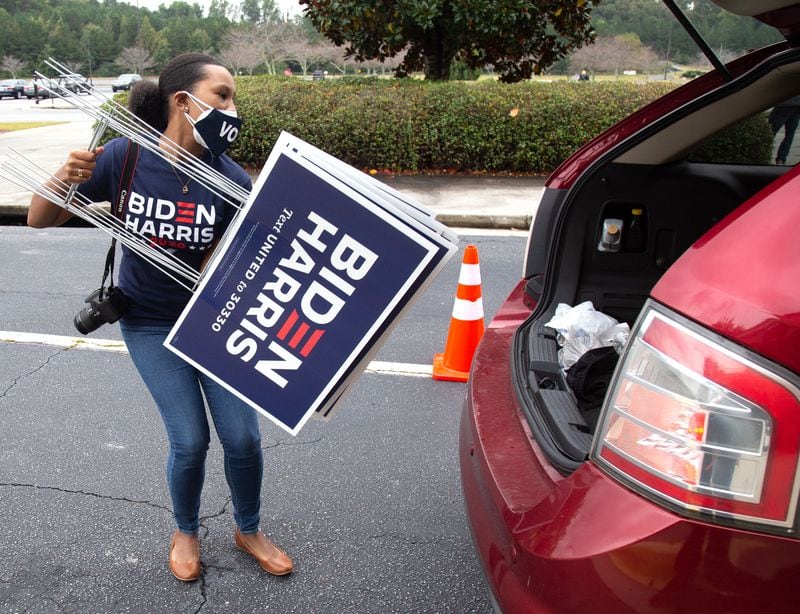 
Volunteer Allison Slocum loads campaign signs into a car at a yard signs giveaway at the New Birth Missionary Baptist Church in Stonecrest Saturday, October 10, 2020.  STEVE SCHAEFER / SPECIAL TO THE AJC 