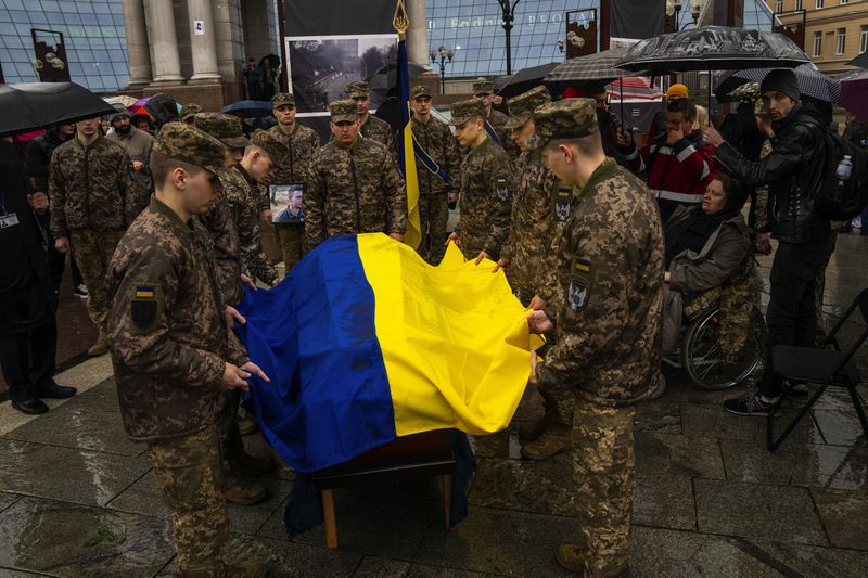 Honor guards salute place an Ukrainian flag onto the coffin of Ukrainian army paramedic Nazarii Lavrovskyi, 31, killed in the war, during his funeral ceremony at Independence square in Kyiv, Wednesday, April 24, 2024. Lavrovskyi, who served in the 244th battalion of the 112th Separate Territorial Defense Brigade, was killed April 18 while helping to evacuate wounded troops from the frontline in the Kharkiv area of eastern Ukraine. (AP Photo/Francisco Seco)