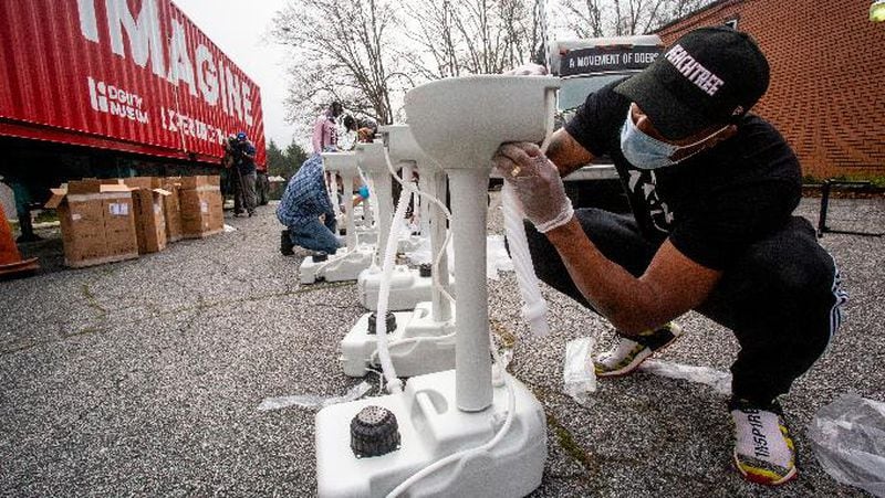 Grammy award-winning hip hop recording artist Lecrae assembles a portable wash station on Thursday, March 19, 2020 in College Park, Georgia. The wash stations were distributed by Lecrae and volunteers with Love Beyond Walls, a non-profit, throughout Atlanta in areas with a high density of homeless persons. (AP Photo/ Ron Harris)