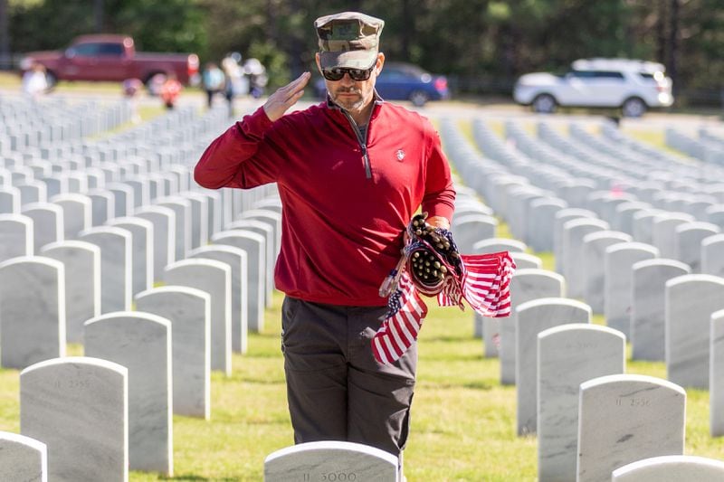 Jeff Smith salutes after placing a flag in front of a tombstone at the Georgia National Cemetery in Canton Saturday, May 27, 2023. Volunteers will place an estimated 21,000 flags on tombstones during the ceremony.  (Steve Schaefer/steve.schaefer@ajc.com)