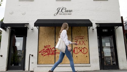 In this April 29, 2020, file photo, a woman walks past a boarded up J. Crew storefront along 14th Street in Northwest Washington. The parent company of clothing chain J. Crew has filed for Chapter 11 bankruptcy, yet another casualty of the coronavirus pandemic. (AP Photo/Andrew Harnik, File)