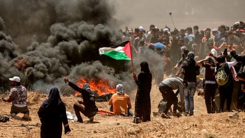 A Palestinian woman holding her national flag looks at clashes with Israeli forces near the border between the Gaza strip and Israel east of Gaza City on May 14, 2018, as Palestinians protest over the inauguration of the U.S. embassy following its controversial move to Jerusalem.