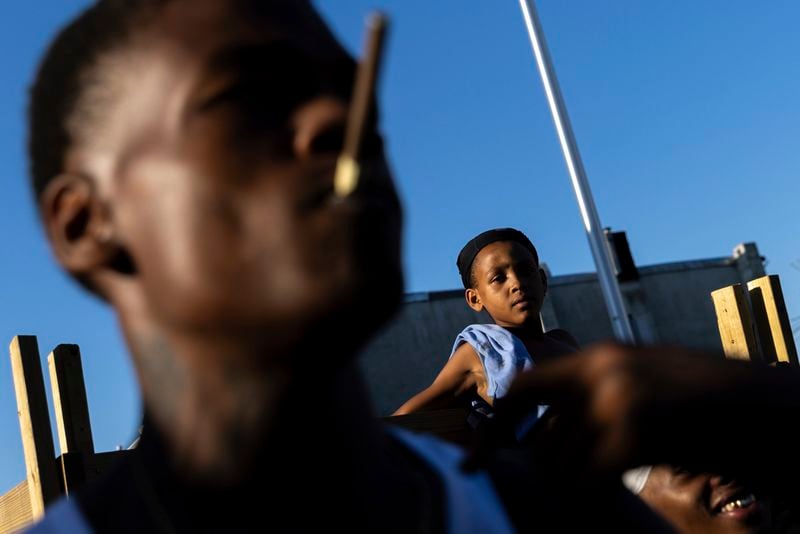 HOLD FOR STORY. People look on as police officers question a boy during a vigil for Antonio Lee, Friday, Aug. 18, 2023, in Baltimore. Lee, 19, was shot and killed while squeegeeing in Baltimore. (AP Photo/Julia Nikhinson)