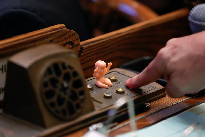 A Mardi Gras king cake baby sits on the desk of Sen. Mike Dugan (R-Carrollton) as he presses the button to vote for a bill on Crossover Day at the State Capitol on Monday, March 6, 2023. (Natrice Miller/ Natrice.miller@ajc.com)