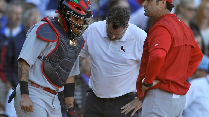St. Louis Cardinals catcher Yadier Molina left, is examined by a trainer while manager Mike Matheny looks on after Molina sprained his thumb while tagging out Chicago Cubs' Anthony Rizzo out at home plate during the eighth inning of a baseball game Sunday, Sept. 20, 2015 in Chicago. St. Louis won 4-3. (AP Photo/Paul Beaty)