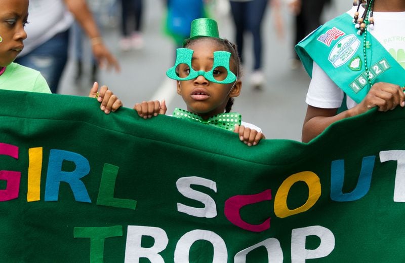 Kala Halet (center) holds up a Girl Scouts banner while marching in the Atlanta St. Patrick's Parade on Peachtree Street on Saturday, March 17, 2018.  STEVE SCHAEFER / SPECIAL TO THE AJC