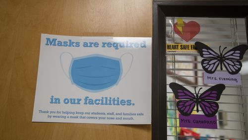 A sign requiring visitors to wear a face mask is displayed on the decorative front door to the Mill Creek High School clinic in Hoschton, on Feb. February 19, 2021. (Alyssa Pointer / Alyssa.Pointer@ajc.com)