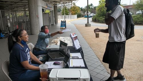 DeKalb County election officials Nytia Harris, from left, and Lamashia Davis work to spread information and share a voter registration application with Christoper Brooks at the Chamblee MARTA station.  (Jenni Girtman for The Atlanta Journal-Constitution)