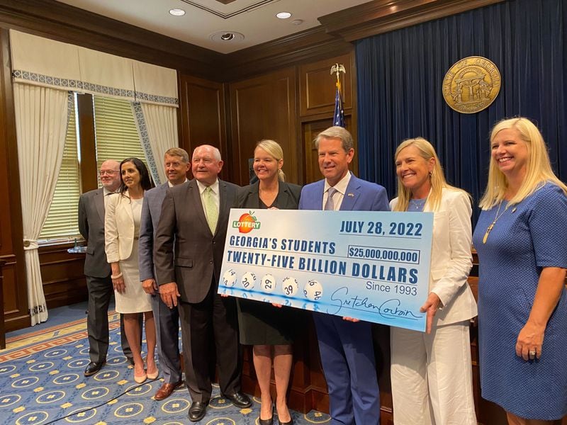Gov. Brian Kemp holds a check representing how much money the Georgia Lottery has raised for education since 1993. Among those with Kemp at the news conference on Thursday, July 28, 2022, are Technical College System of Georgia Commissioner Greg Dozier (third from left), University System of Georgia Chancellor Sonny Perdue (fourth from left), Gretchen Corbin (fifth from left), CEO and president of the Georgia Lottery, and Kemp's wife, Marty (second from right). (Vanessa McCray / Vanessa.McCray@ajc.com)