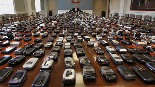 Dec. 20, 2011: Corrections Commissioner Brian Owens, sitting at a table holding more than 1,000 confiscated cellphones, talks about the threat and danger of the phones in prisons. (AJC file / Vino Wong)