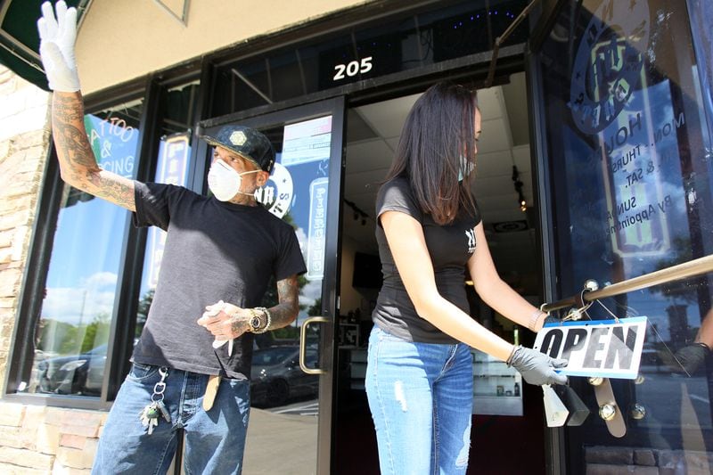 Holly Bernard, the owner of No Regrets Tattoo Shop in Loganville, fixes the open sign outside her shop on Friday. Miguel Martinez for the Atlanta Journal-Constitution