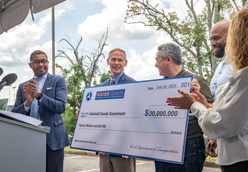 Assistant Secretary of Transportation Christopher Coes, from left, participates with Lewis Cooksey, director of the Gwinnett Department of Transportation, and Ben Ku and others in the ceremonial check presentation of a $20 million federal grant Monday, July 24, 2023 awarded to transform the transit center just west of Gwinnett Place Mall.  (Jenni Girtman for The Atlanta Journal-Constitution)