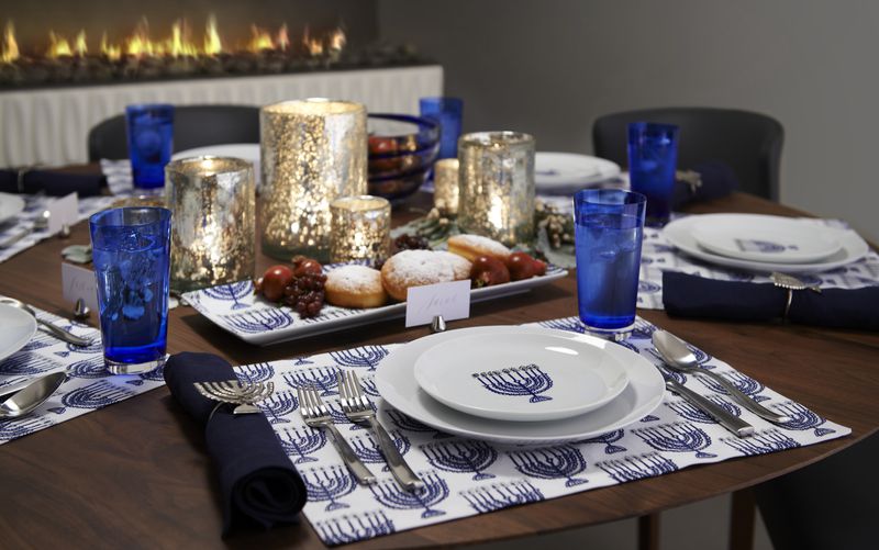 The tablescape from Crate and Barrel blends traditional Hanukkah blue and white and menorah-themed plates and table accents. Bubbled silver glass candle holders and cobalt blue glassware add elegance to an otherwise casual setting.