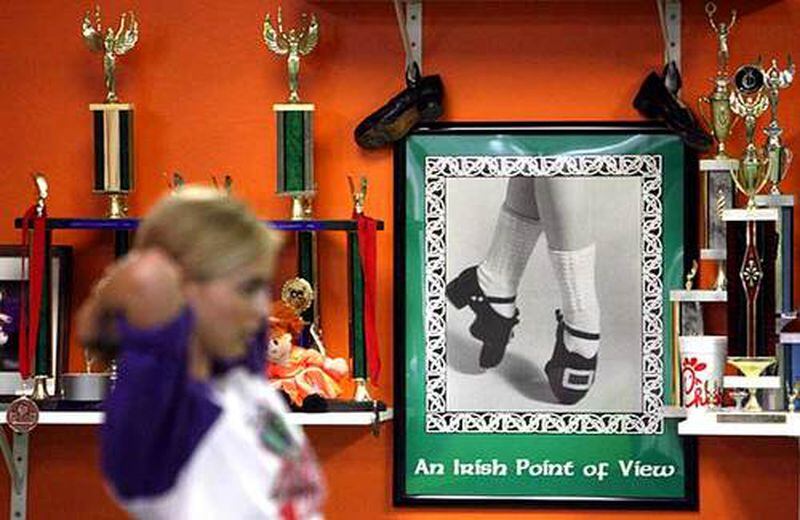 Catie Foley, 15, of Alpharetta ties up her ponytail beside some of the trophies that teacher Karl Drake has won over the years at the Drake School of Irish Dance in Norcross. The group has traveled to Belfast for competitions.