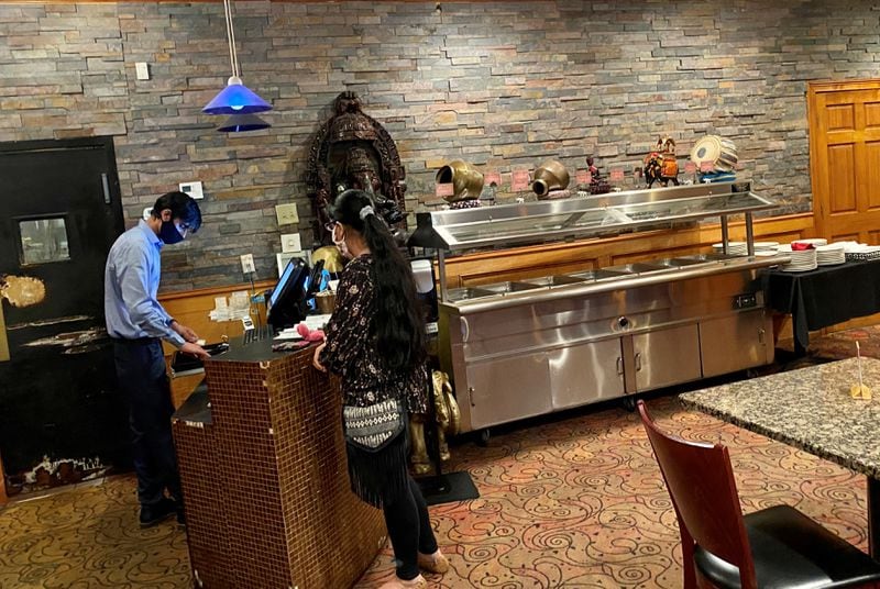 A customer picks up a takeaway order at Cafe Bombay on Briarcliff Road, where the lunchtime steam tables are empty, thanks to COVID-19 restrictions.  Wendell Brock for The Atlanta Journal-Constitution