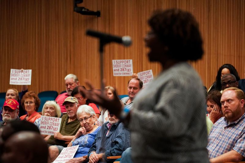 Supporters of the Immigration and Customs Enforcement agency's 287(g) policy, are seen behind opponent Glory Kilanko, of Snellville, as she speaks during a community engagement discussion on immigration organized by Gwinnett Commissioner Marlene Fosque at the Gwinnett Justice and Administration Center on Wednesday, July 31, 2019, in Lawrenceville. ELIJAH NOUVELAGE/SPECIAL TO THE AJC