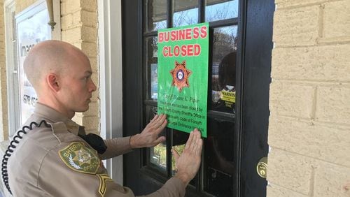 A Forsyth County deputy puts a closure notice up at one of two Forsyth County massage parlors shut down under the county ordinance that took effect early last year. CONTRIBUTED