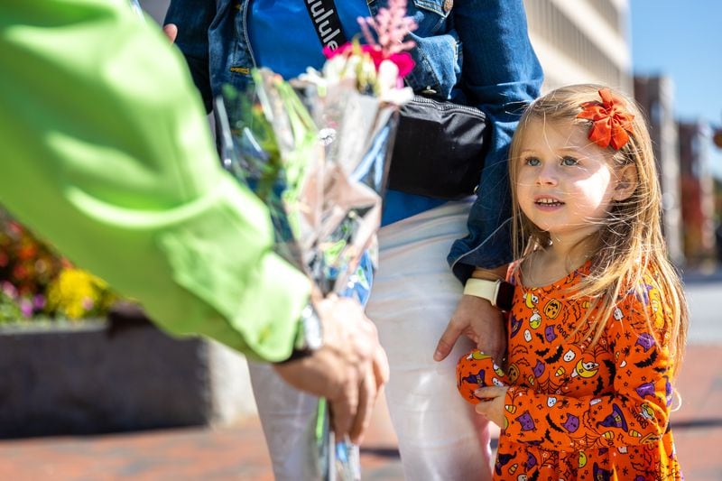 Florist K. Mike Whittle hands Meredith Williams, 4, a free flower bouquet in Marietta Square in Marietta on Wednesday, October 18, 2023. The event was part of the Society of American Florists' “Petal it Forward” goodwill initiative. (Arvin Temkar / arvin.temkar@ajc.com)