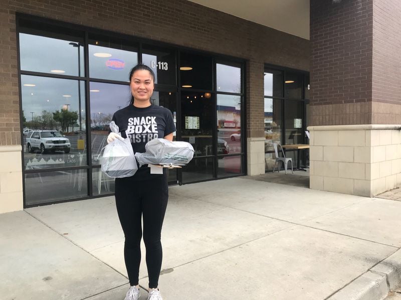 Snackboxe Bistro employee Jennifer Athakhanh brings an order out for curbside pickup. The Laotian restaurant in Doraville currently does not allow customers to enter the building. LIGAYA FIGUERAS / LIGAYA.FIGUERAS@AJC.COM