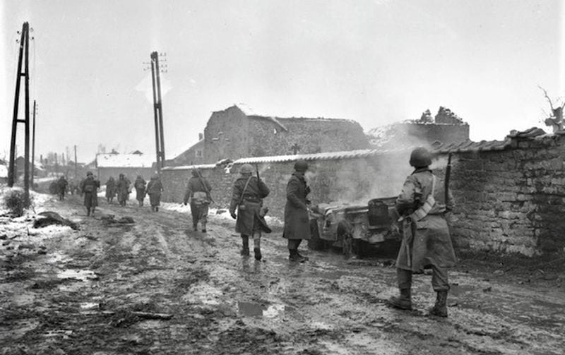 Infantrymen move along a road through Beffe, Belgium, which was hit by Nazi mortars.  The jeep at right was hit by shell.  Belgium.  1/5/45.  290th Regt. 75th Div.