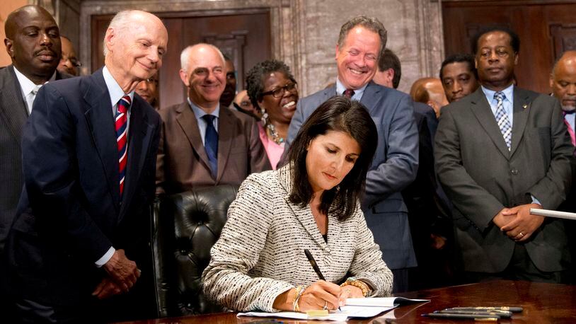 In this July 9, 2015 file photo, South Carolina Gov. Nikki Haley signs a bill into law as former South Carolina governors and officials look on, at the Statehouse in Columbia, S.C. The law enables the removal of the Confederate flag from the Statehouse grounds more than 50 years after the rebel banner was raised to protest the civil rights movement. Behind Haley is former Gov. David Beasley, who fought for the removal of the flag when he was in office in 1996. His proposal infuriated fellow Republicans and voters bounced him from office in 1998. (AP Photo/John Bazemore, File)