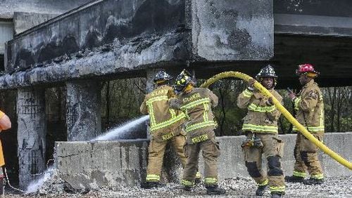 Atlanta firefighters put out a smoldering fire Friday before crews began demolition work following the I-85 bridge collapse. JOHN SPINK  / JSPINK@AJC.COM