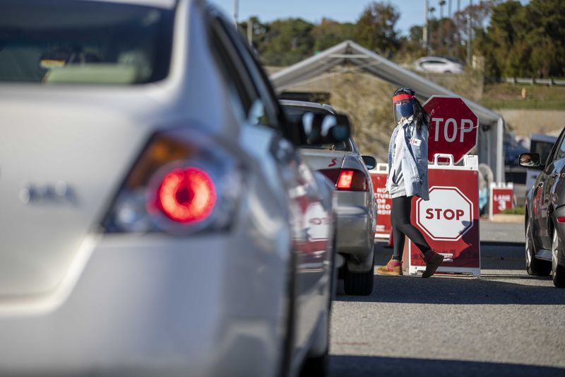 Workers walk up and down a line of cars to gather personal information before administering COVID-19 tests at a DeKalb County drive-thru testing site in Doraville.  (Alyssa Pointer / Alyssa.Pointer@ajc.com)