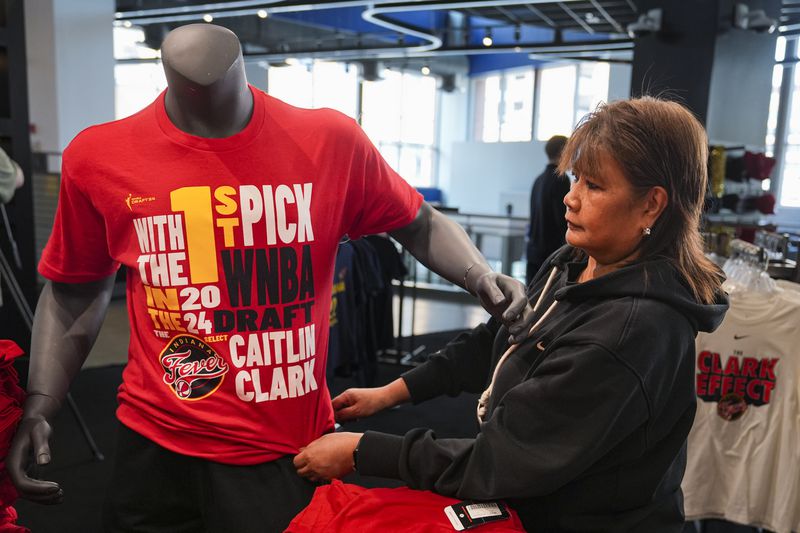 Editha Sison adjusts the shirt on a mannequin featuring Caitlin Clark in the Indiana Fever team store in Indianapolis, Tuesday, April 16, 2024. The Fever selected Clark Clark as the No. 1 overall pick in the WNBA basketball draft. (AP Photo/Michael Conroy)