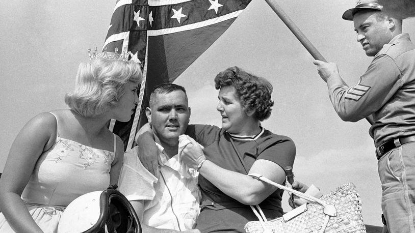 In this Sept. 3, 1962, file photo, a confederate flag waves behind Junior Johnson as he poses with his sister, right, and Miss Sun Fun U.S.A. in the winner's circle after the Southern 500 auto race at Darlington Speedway. (AP Photo/Perry Aycock, File)