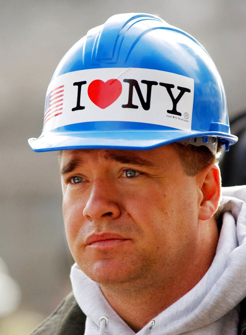 FILE - In this Oct. 11, 2001 file photo,  with an "I Love NY" sticker on his hardhat, New York City firefighter Kevin Bohan pauses at a memorial service near ground zero in New York.  Milton Glaser, the designer who created the "I (HEART) NY" logo and the famous Bob Dylan poster with psychedelic hair, has died. He died Friday, his 91st birthday.AP Photo/Stan Honda, pool, File)
